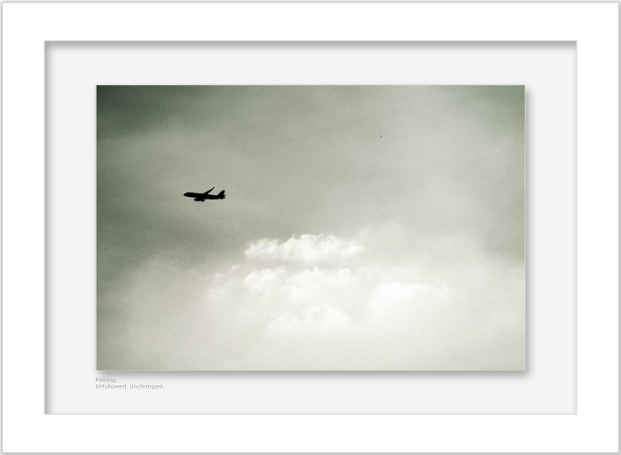 Framed minimal photograph of airplane flying across cloudy sky displayed on wall